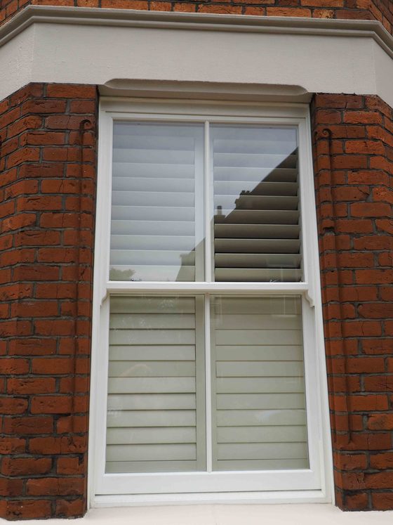 White sliding sash window with plantation shutters in a brick bay